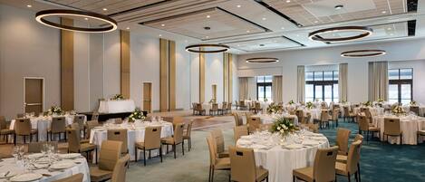 Une salle de banquet spacieuse, avec des tables rondes, des chaises de couleur beige et un sol recouvert de moquette.