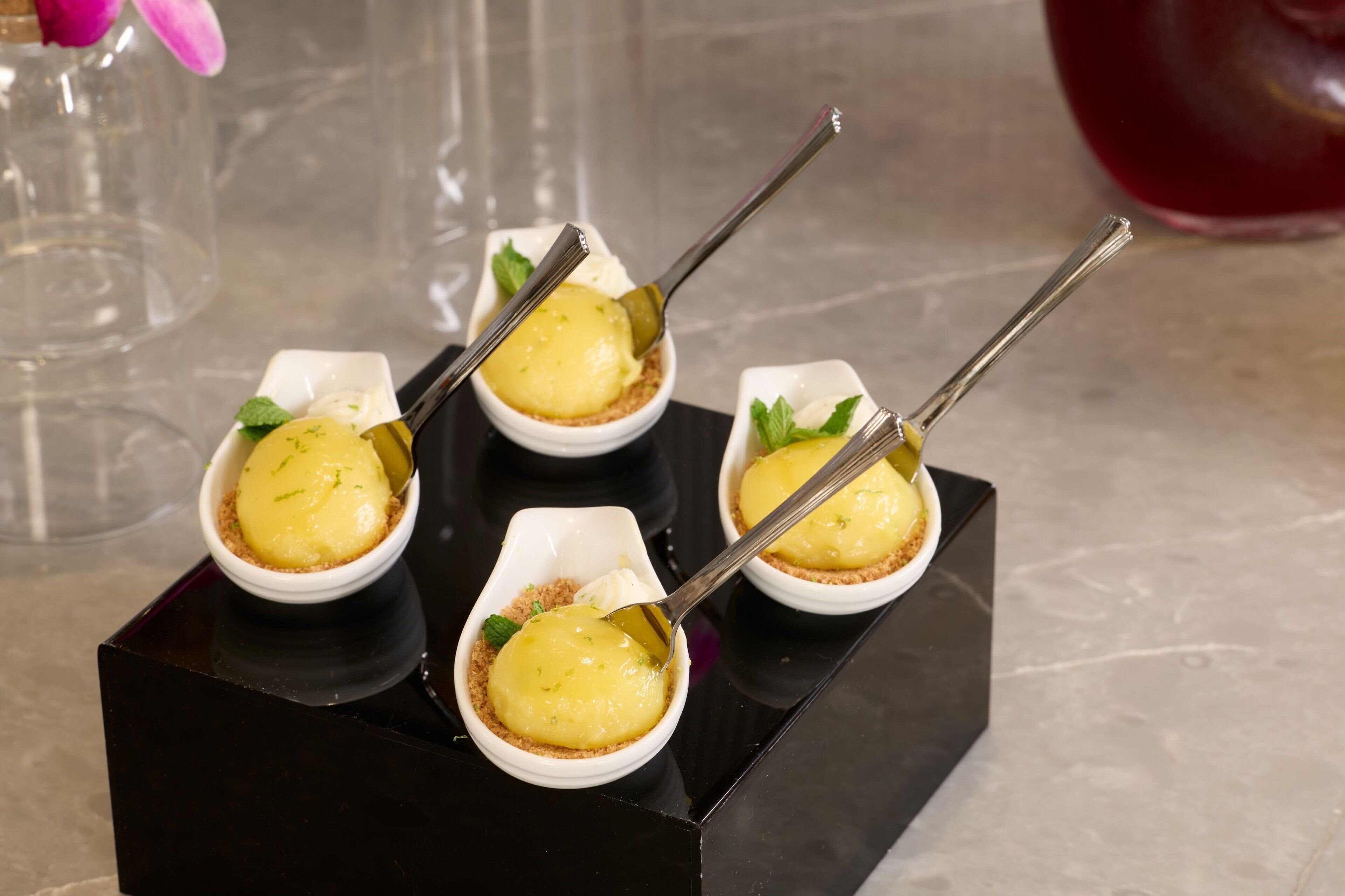 Quatre petits bols blancs contenant un dessert jaune, le tout posé sur une base noire.