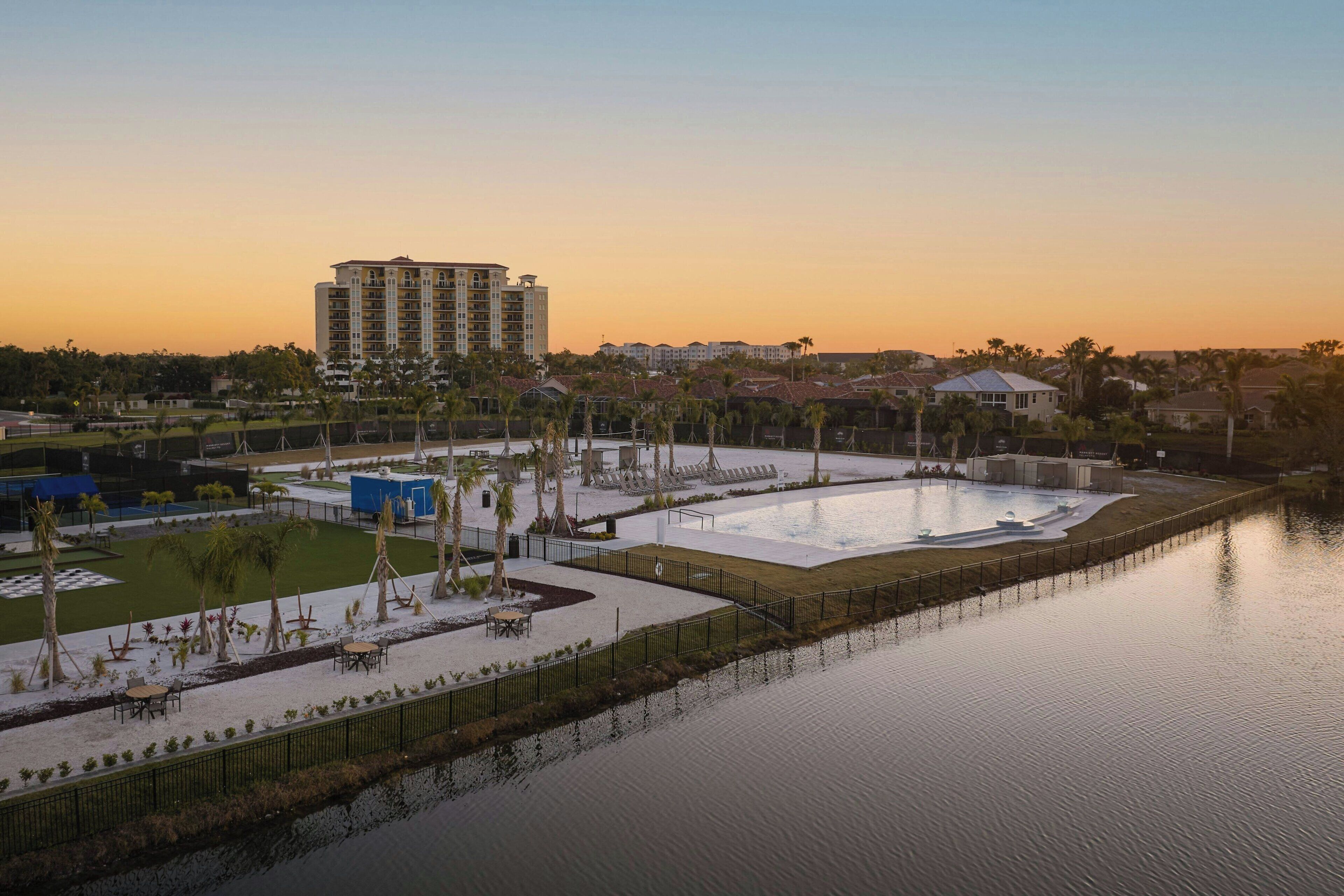Un complexe hôtelier doté d’une grande piscine, de palmiers et d’un bâtiment visible au loin.