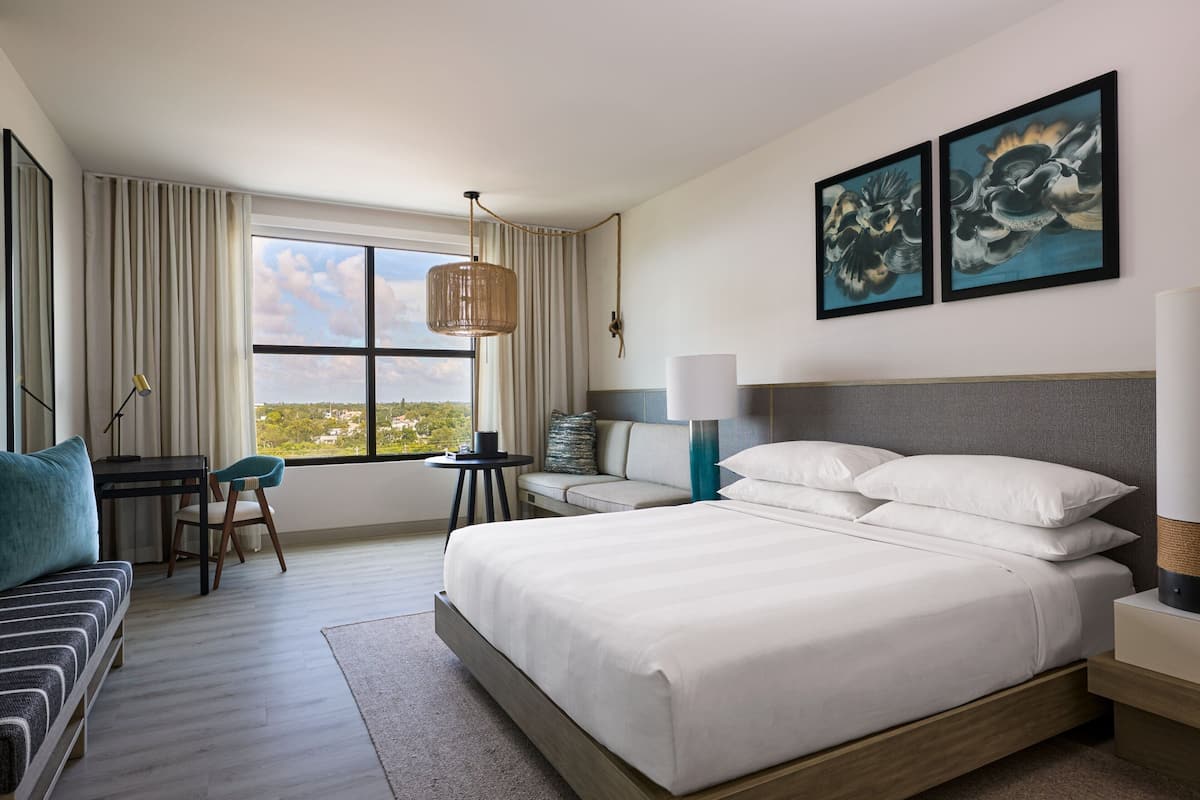 A modern hotel room with a large bed, a desk, and a view of the city.