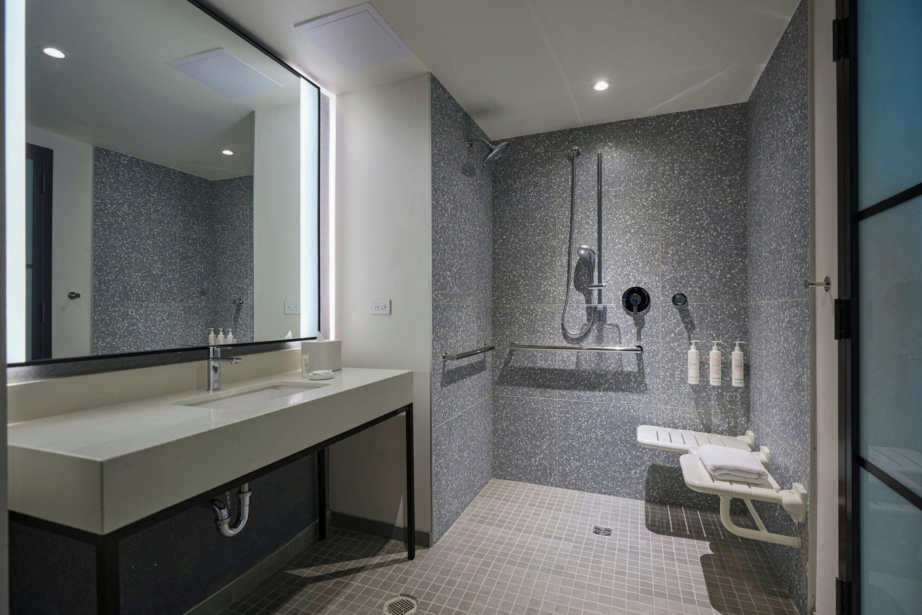 A modern bathroom with a large mirror, a sink, a shower, and a bench.