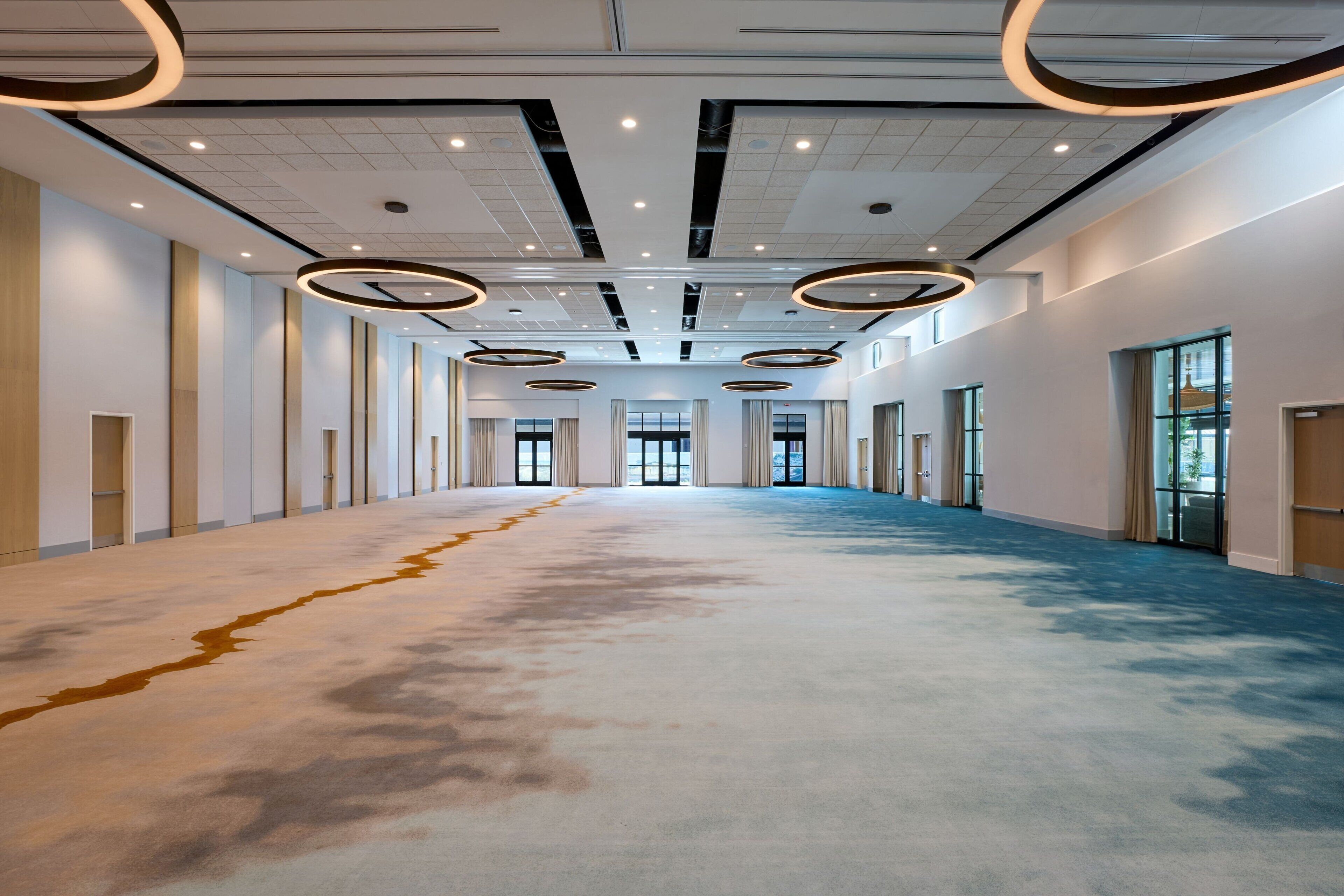 A spacious, well-lit hallway with a carpeted floor, large windows, and a modern ceiling design.