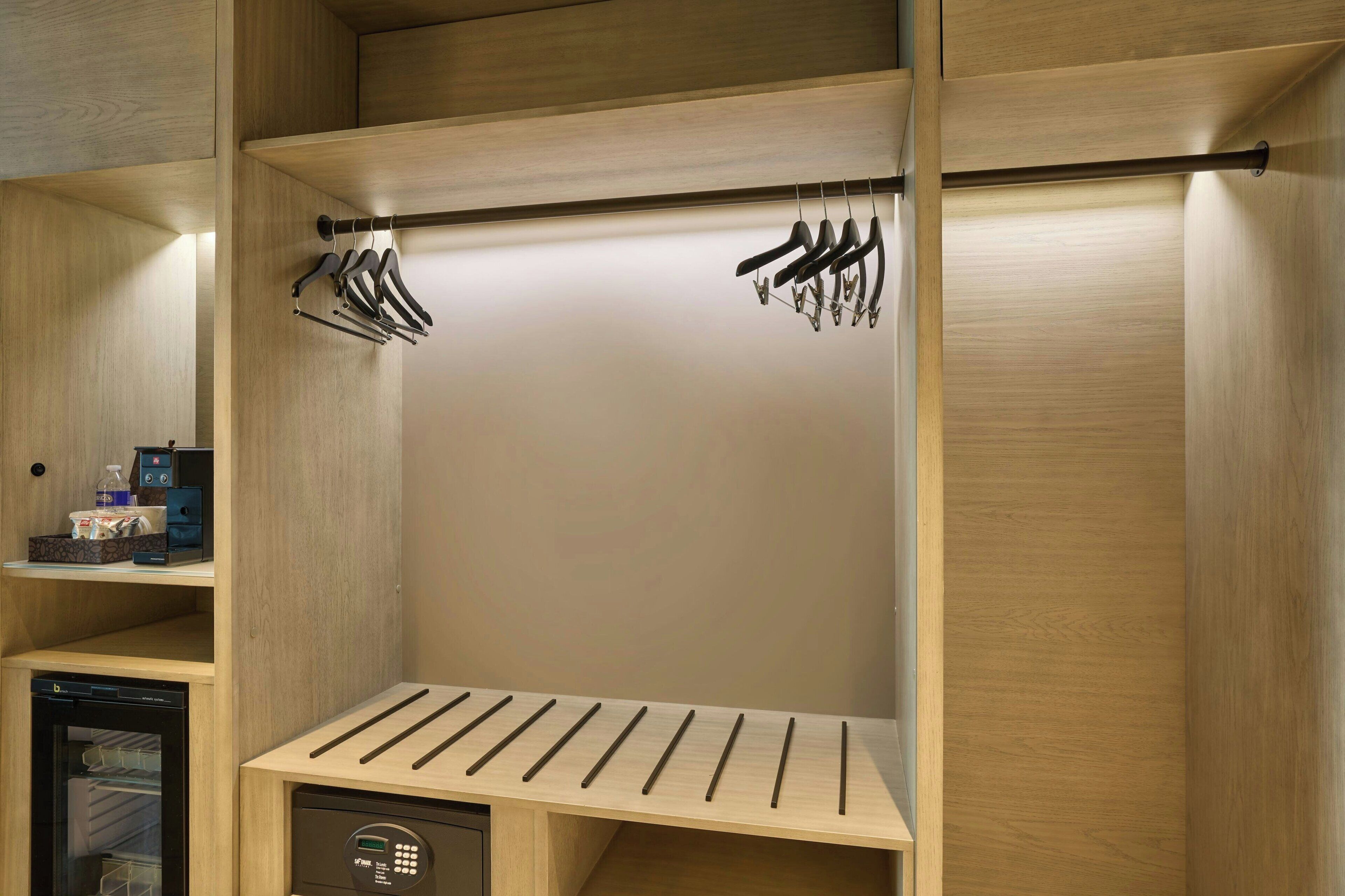 Un armario compacto y moderno con estantes de madera, una barra para colgar y un electrodoméstico integrado.
