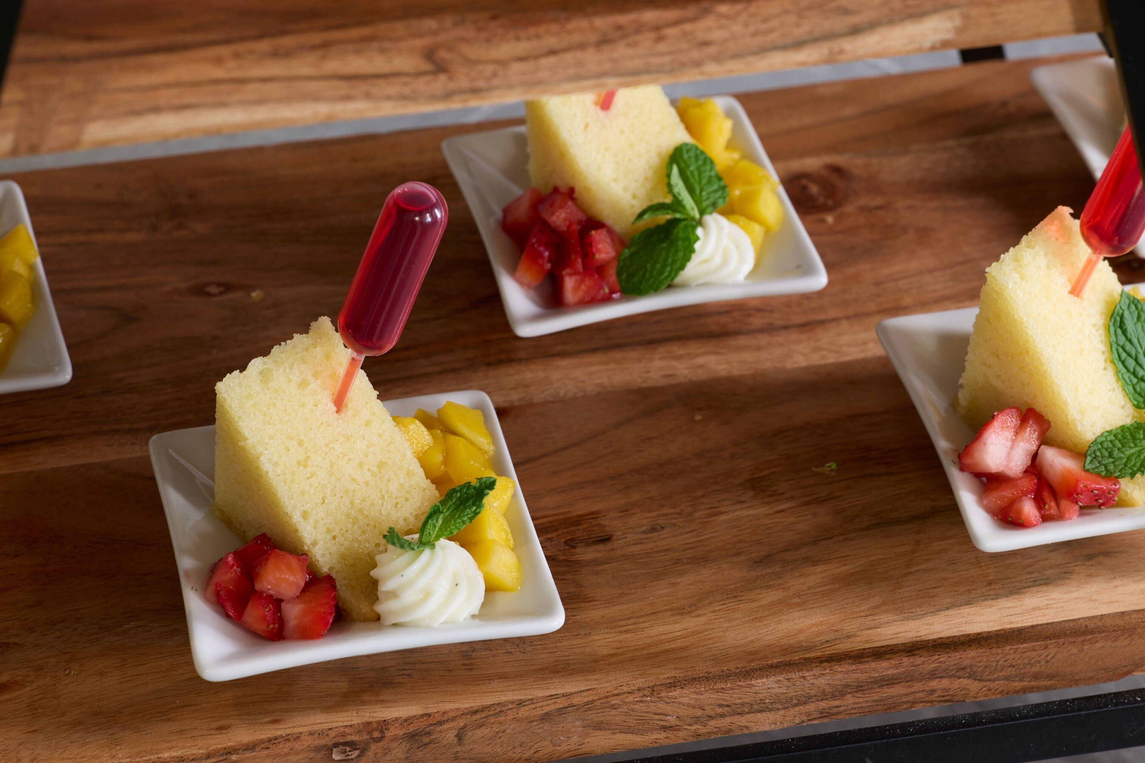 A dessert tray with slices of cake, strawberries, whipped cream, and mint leaves on a wooden table.