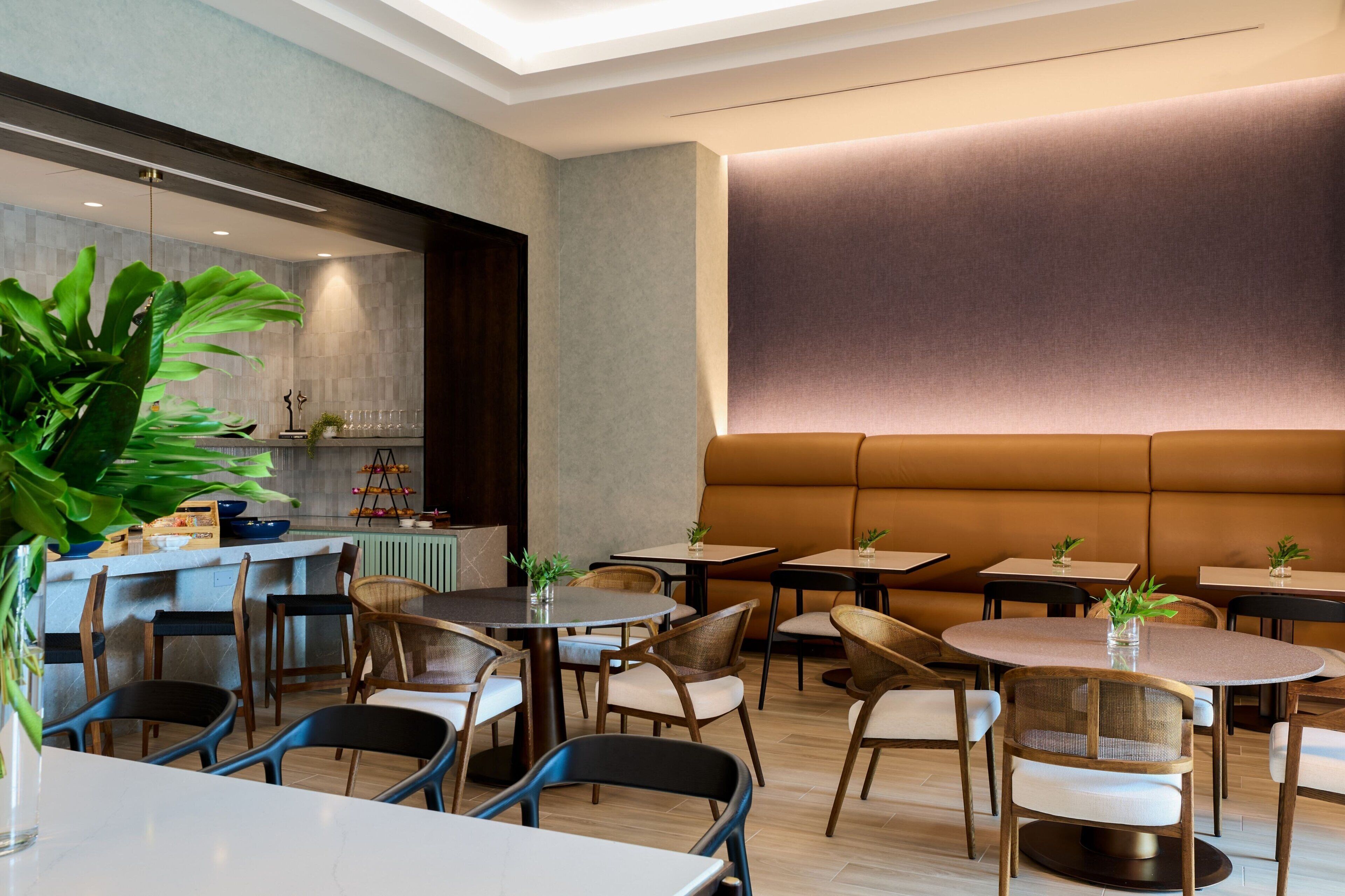A modern dining area with round tables and chairs, a central bar area, and a large cushioned bench.