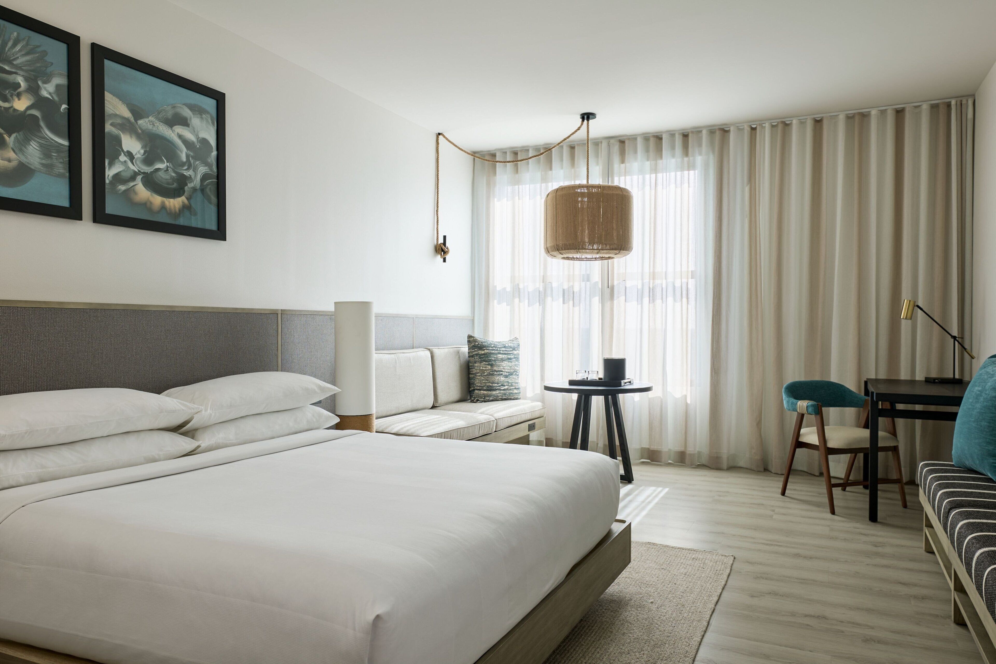 Quarto de hotel moderno com uma cama grande, um sofá, uma escrivaninha e um candeeiro pendente.