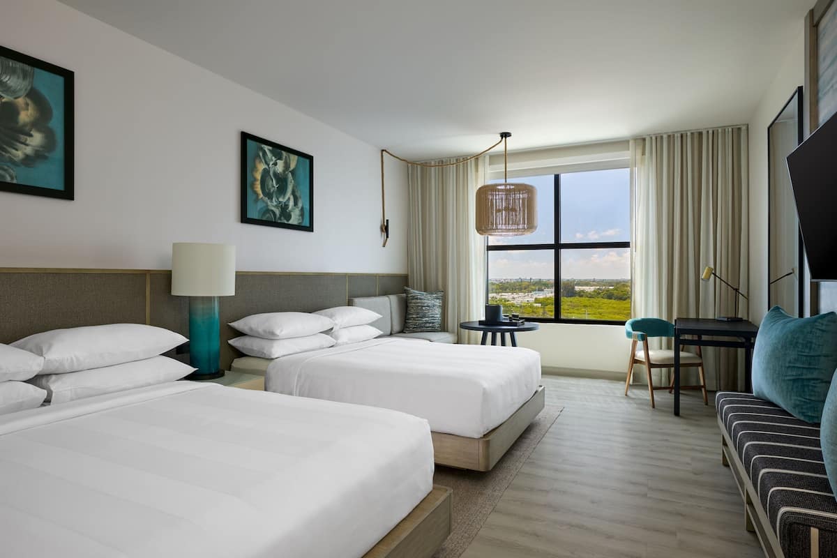 A hotel room with two beds, a sofa, a desk, and a large window with a view.
