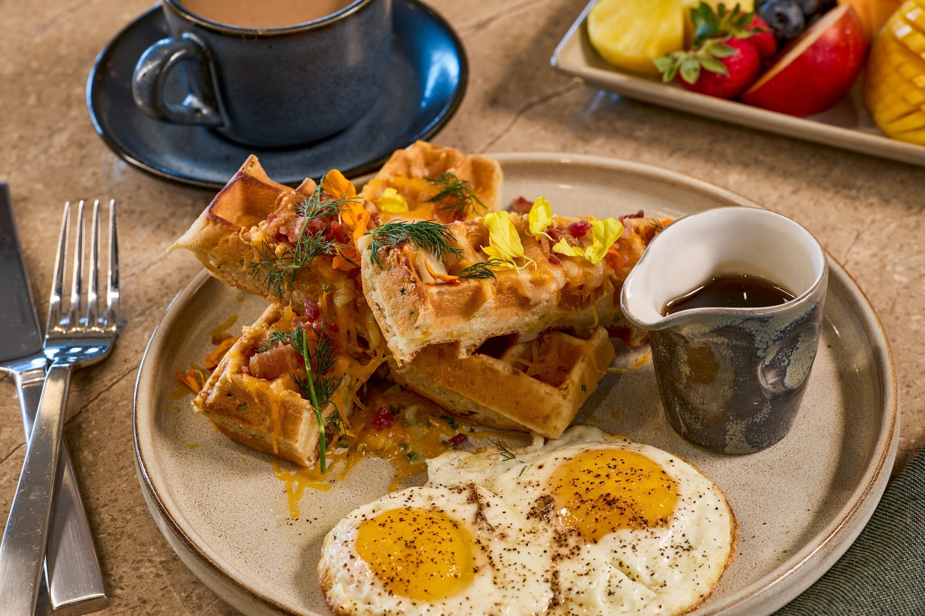 Une assiette de petit-déjeuner avec des gaufres, des œufs et une tasse de café.