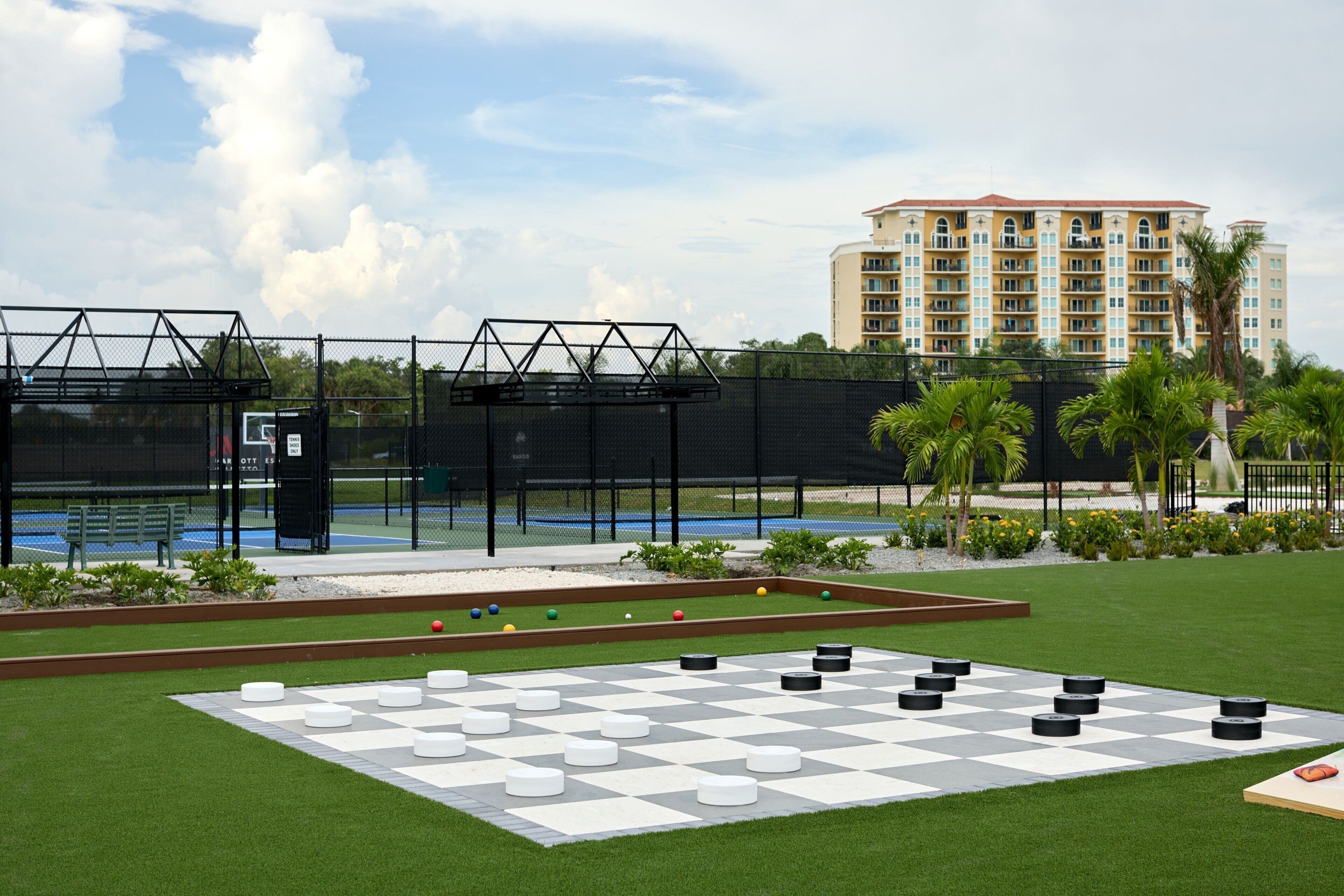 A checkered outdoor area with a pool, palm trees, and a building in the background.