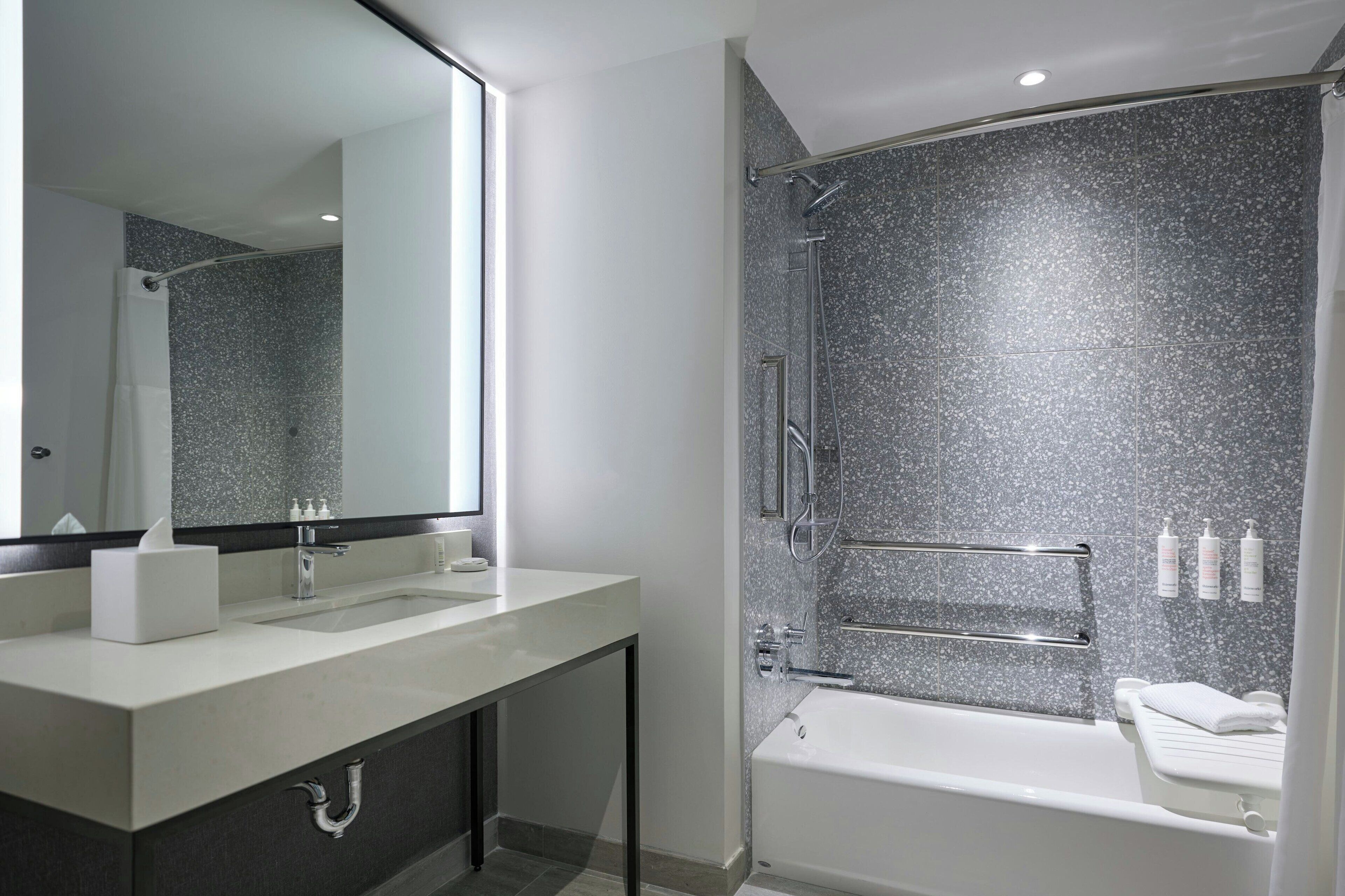 A modern bathroom with a large mirror, two sinks, a shower, and a bathtub.