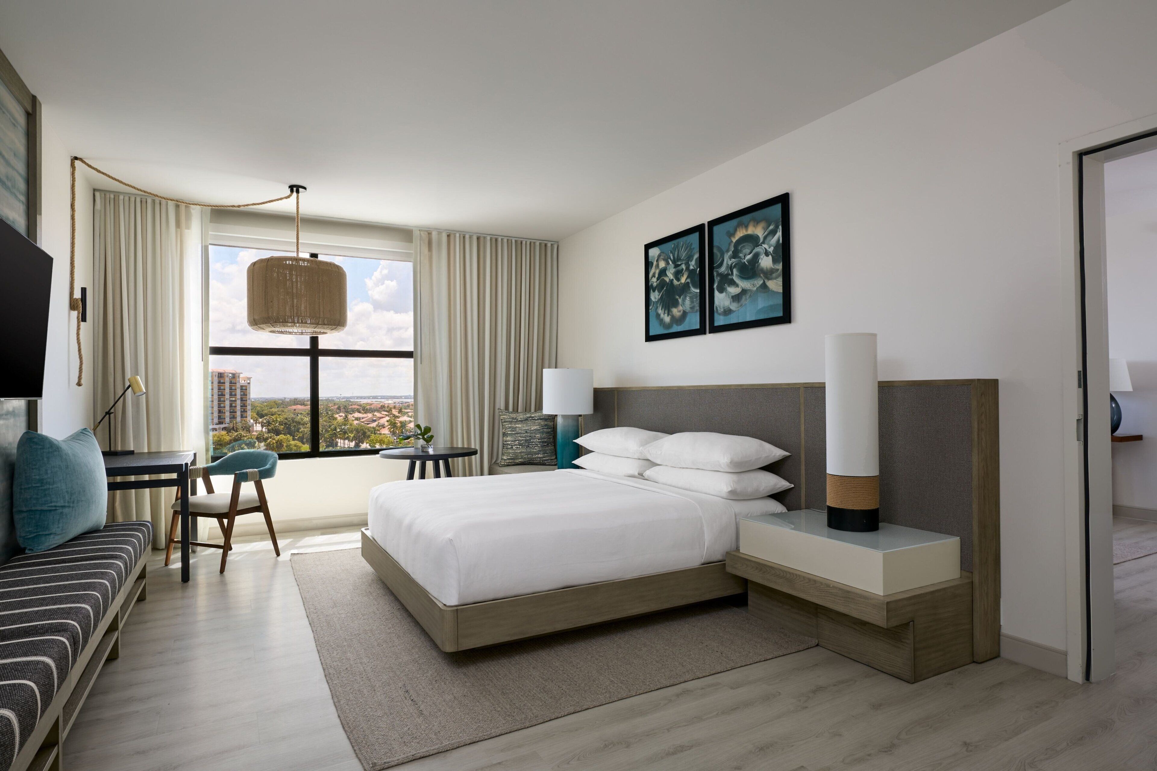 Una habitación de hotel moderna con una cama grande, un escritorio, una silla y vistas a la ciudad.