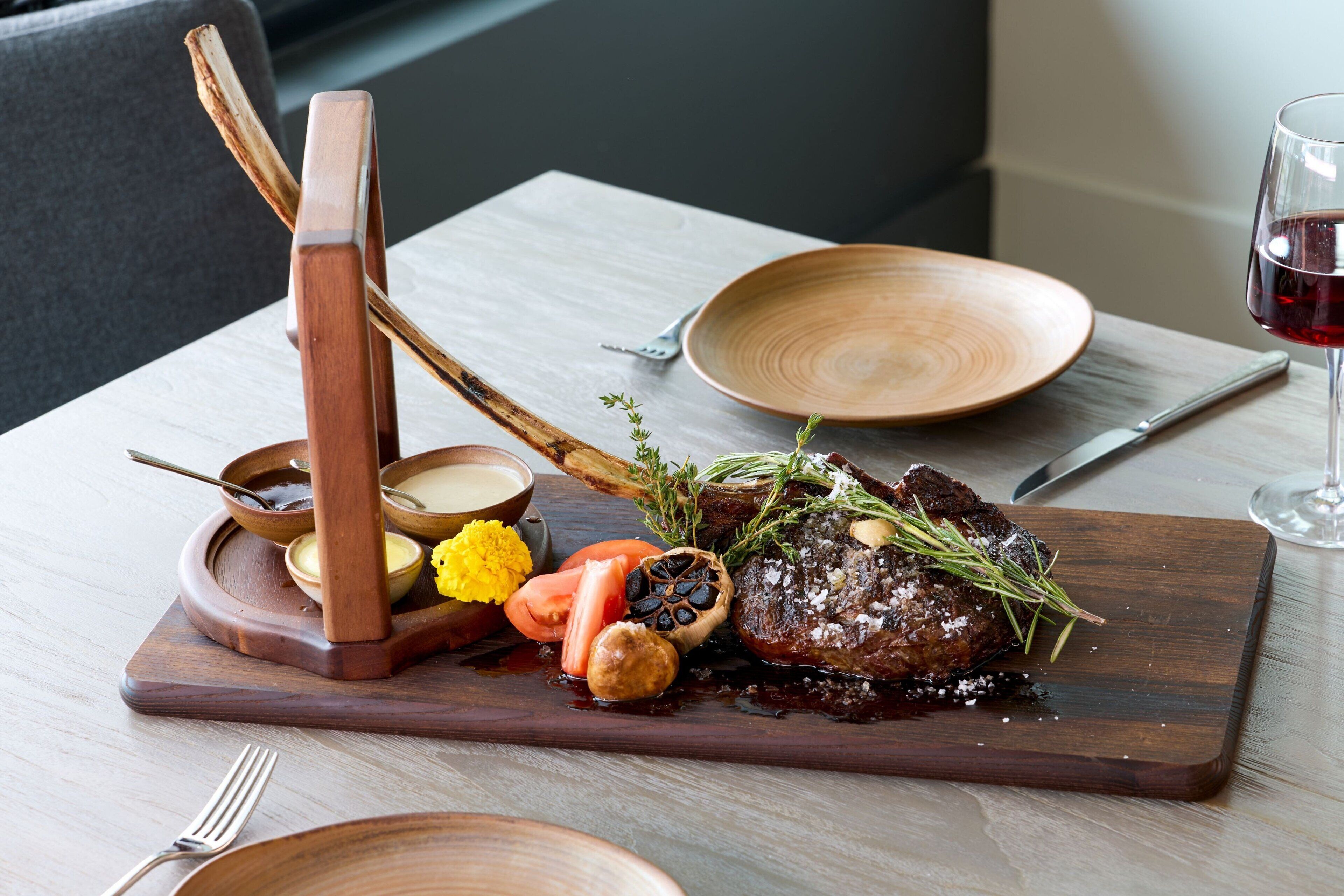 Una tabla de madera con un bistec, verduras y condimentos sobre una mesa.