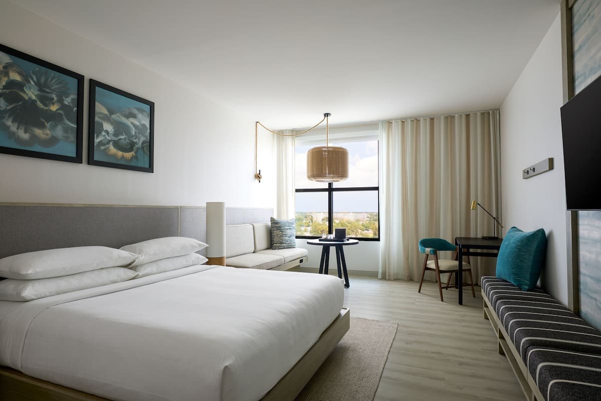A modern hotel room with a large bed, a sofa, a small table, and a window with curtains.