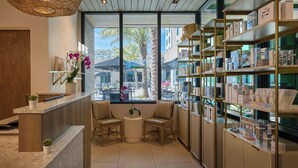 A reception area with a marble counter, two chairs, a small table with a plant, and a shelf with products. - Palmetto Marriott Resort & Spa (Palmetto)