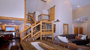 A spacious living area with a wooden staircase, a dining table, and a modern kitchen in the background.