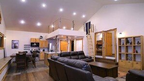 A spacious living area with a dining table, sofas, a kitchen, and a loft with a railing.