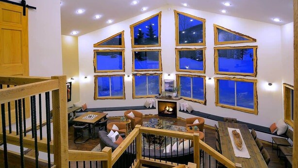 A cozy living room with a fireplace, multiple windows, and a staircase.