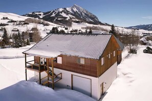 Une cabane en bois avec un balcon, un garage et une vue sur une montagne enneigée.