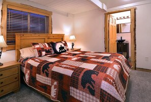 Une chambre à coucher avec une tête de lit en bois, une couvre-lit matelassée, une table de chevet avec une lampe et une fenêtre avec des stores.
