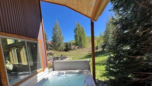 A hot tub under a wooden pergola with a clear view of surrounding trees and a hillside.
