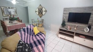 Una sala de estar con sofá, mesa de comedor, sillas, televisor y un pequeño árbol de Navidad.