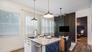 Une cuisine moderne dotée d’un îlot central intégré, d’un coin repas avec un canapé bleu et d’un téléviseur à écran plat fixé au mur.