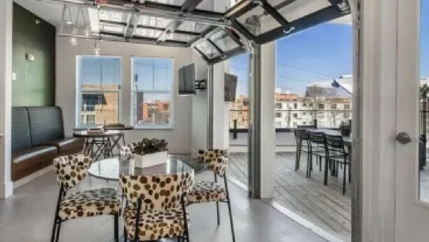 Un intérieur moderne avec un plafond en verre, une table ronde entourée de chaises à motifs léopard, et une vue sur la ville grâce à de grandes fenêtres.