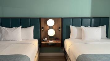Habitación de hotel con dos camas, cabecero de madera, mesita de noche con lámpara y un reloj.