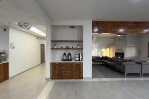 A modern interior with a kitchen area featuring wooden cabinets and a coffee station, and a living area with a sectional sofa and fireplace.