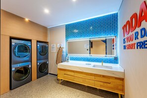 Ein modernes Badezimmer mit einem großen Spiegel, einem Waschbecken und zwei an der Wand montierten Waschmaschinen.