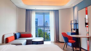 A hotel room with a large bed, a sofa, a small round table, and a chair. There is a large window with curtains and a view of buildings outside. - Holiday Inn Express Beijing Conference Center (Beijing)