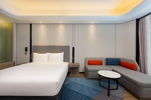 Ein modernes Hotelzimmer mit einem großen Bett, einer Couch, einem kleinen Tisch und einem gemusterten Teppich.