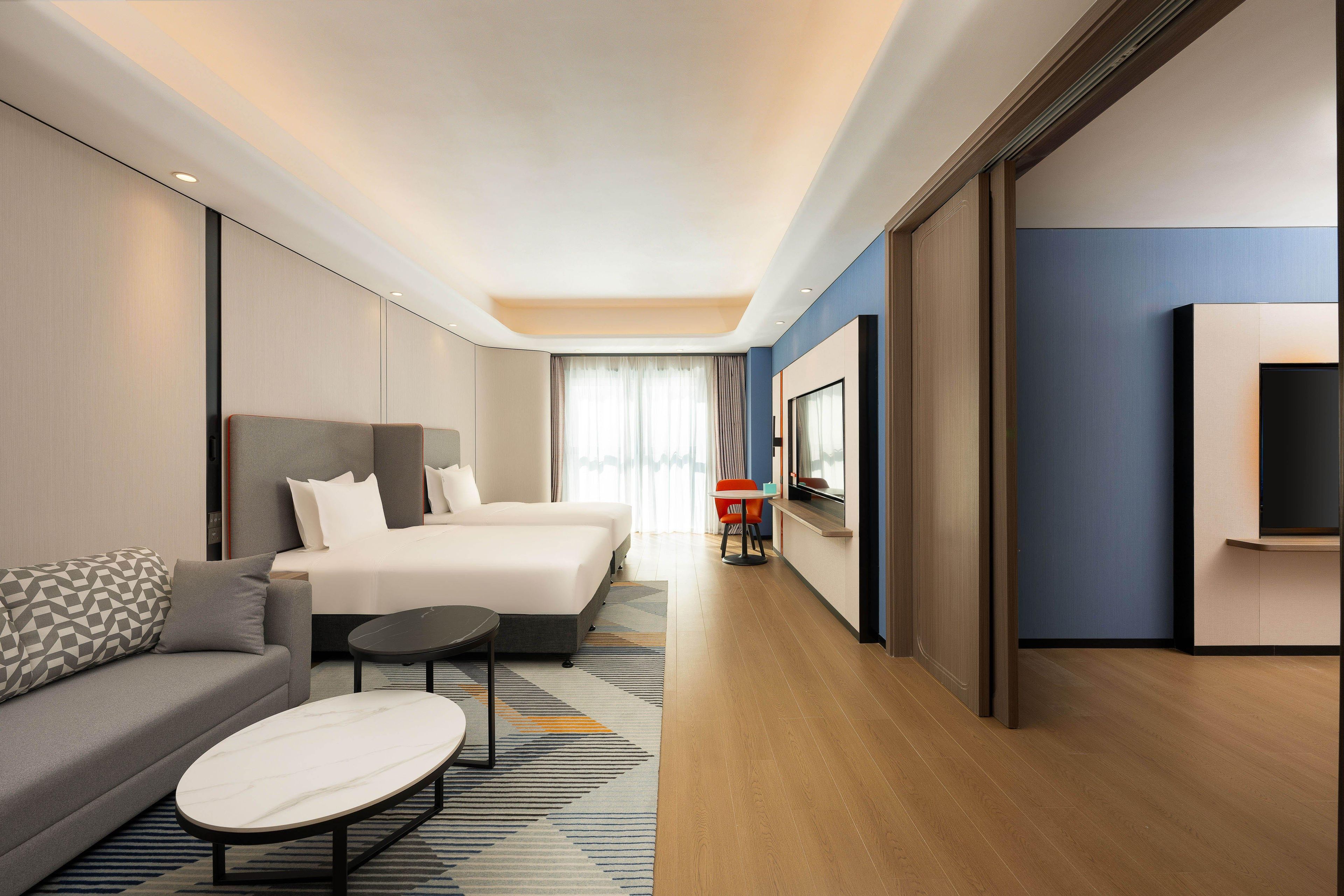 Una habitación de hotel moderna con una cama grande, un sofá, una mesita y un televisor.