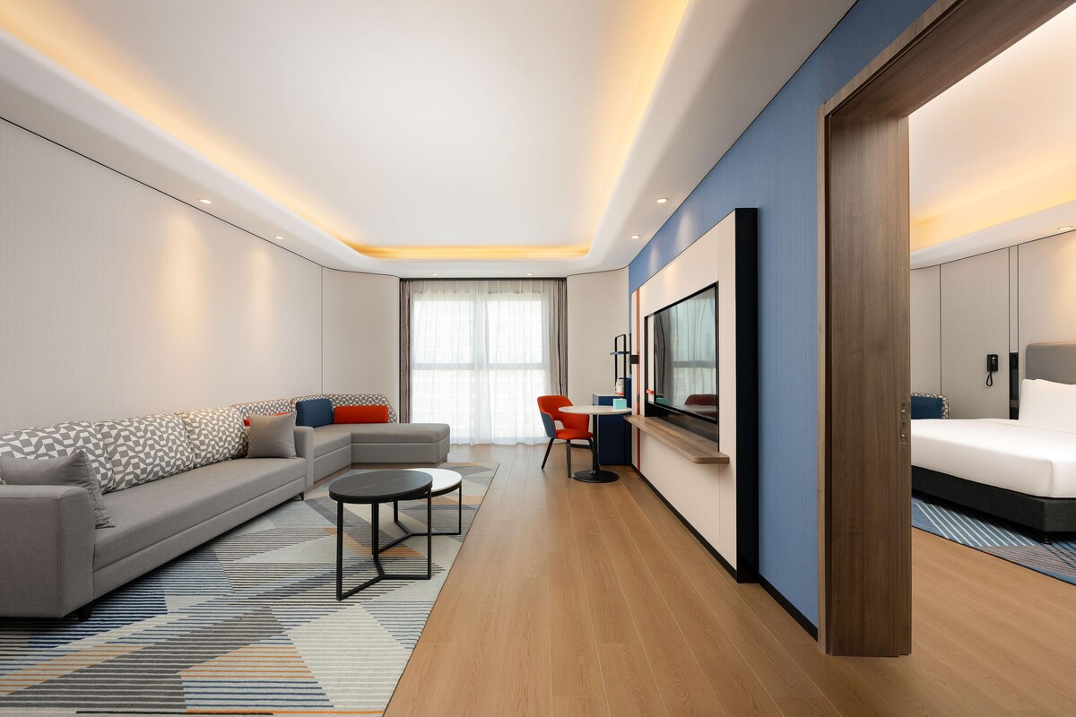 A modern hotel room with a sofa, a dining table, and a bed.