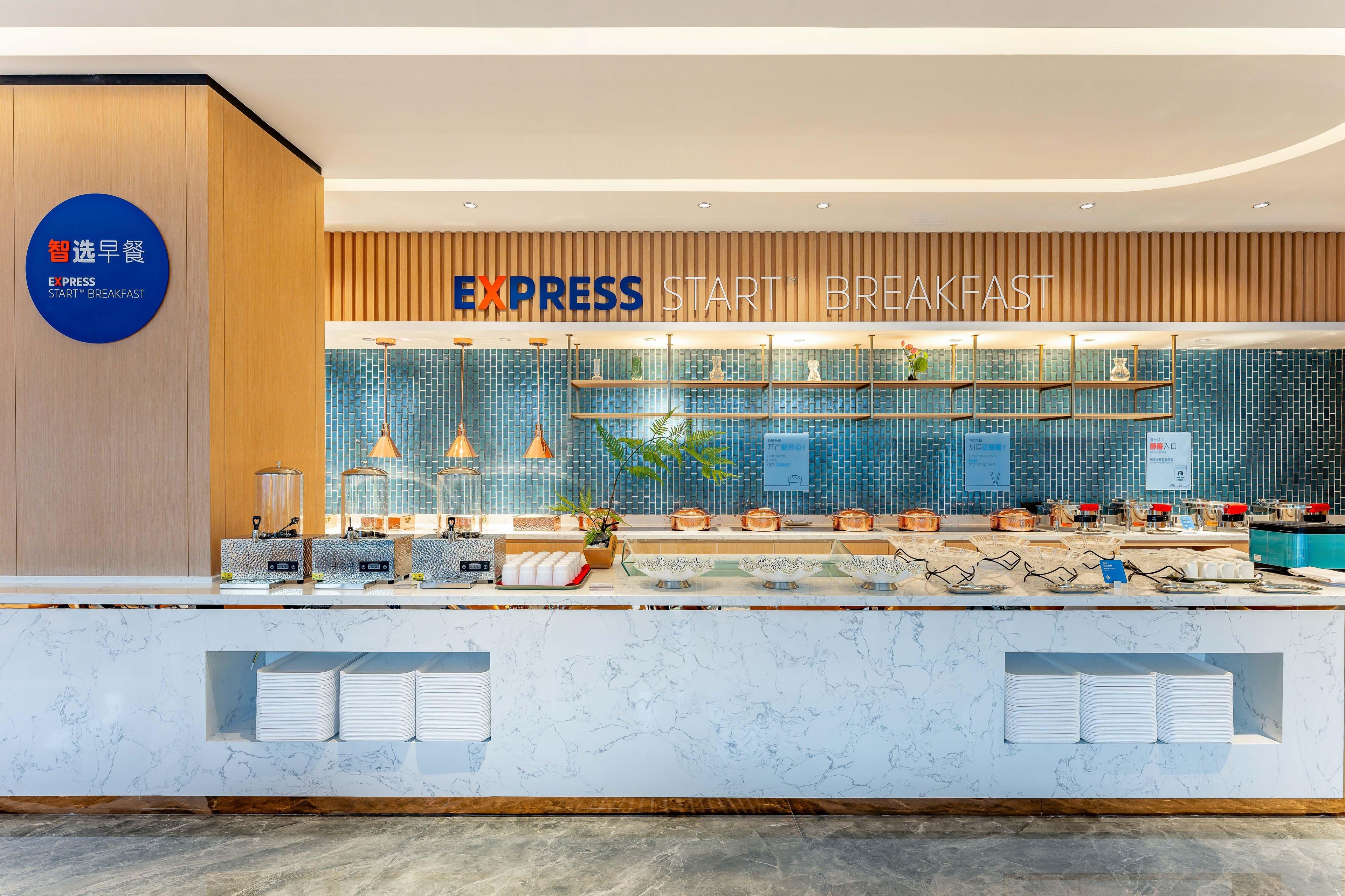 Un moderno espacio para desayuno tipo bufé, con un cartel que dice "EXPRESS START BREAKFAST" y un letrero azul que indica "Smart Breakfast Selection".