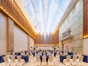 Une grande salle de conférence avec de nombreuses rangées de tables et de chaises, un plafond haut orné de tentures et un mur en marbre.