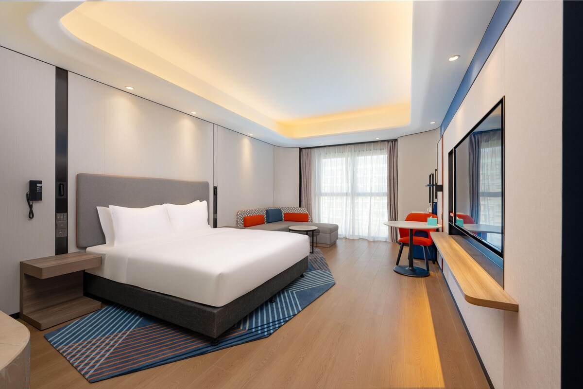 A modern hotel room with a large bed, a desk, and a seating area.