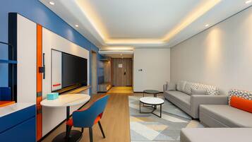 Una habitación de hotel moderna con zona de comedor, sofá y televisor.