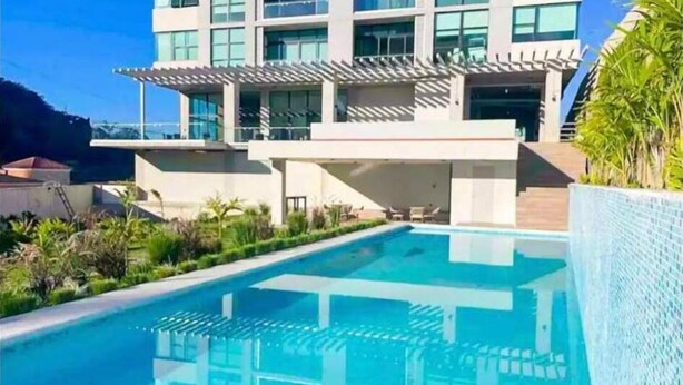 Un hotel moderno con piscina, area salotto esterna coperta e vista sul paesaggio circostante.
