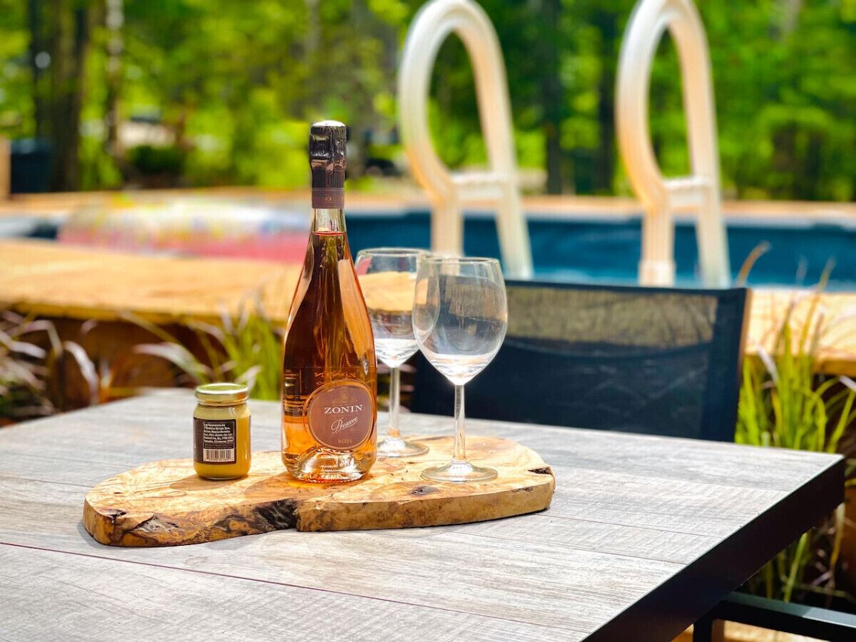 Une bouteille de vin Zonin, deux verres et un pot de miel, le tout posé sur une planche en bois près d’une piscine.