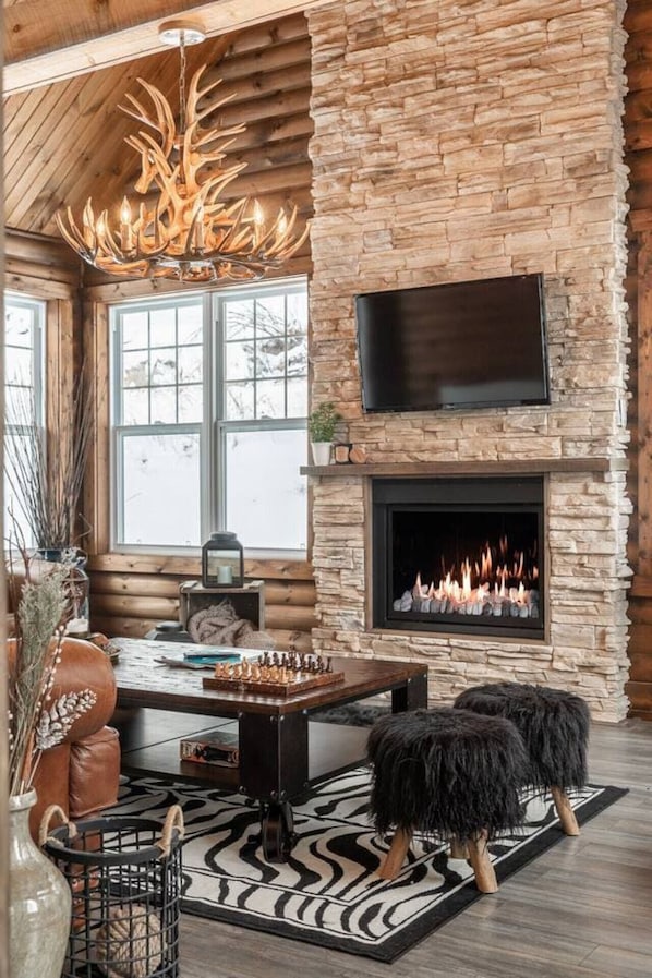 Un interior acogedor con una chimenea de piedra, un televisor de pantalla plana montado encima y un techo de madera.