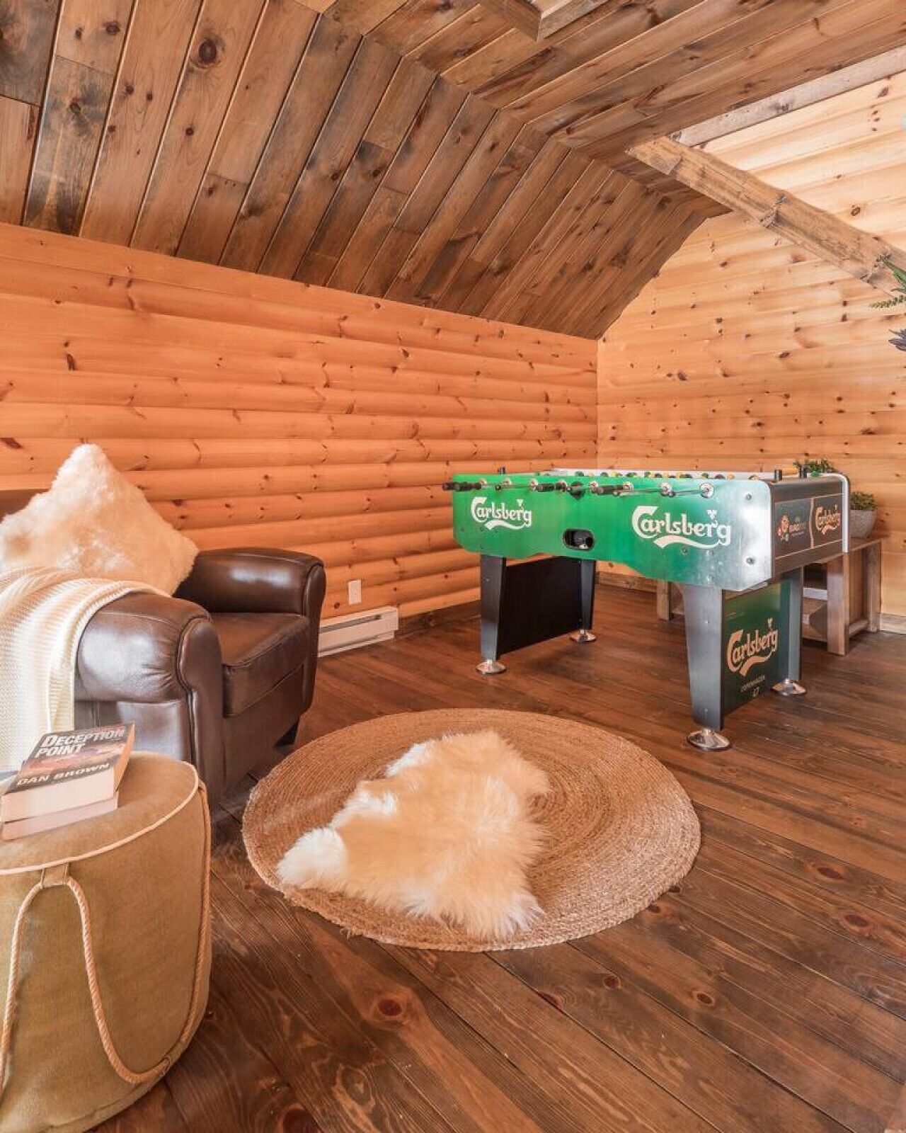 A cozy room with a wooden ceiling, a leather chair, a foosball table, and a fur rug.