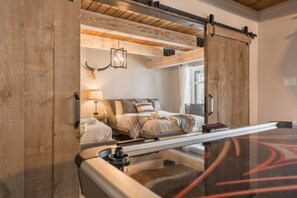 Un dormitorio con cama, mesita de noche, lámpara y techo de madera rústica.