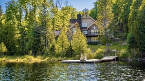 Une maison avec une jetée qui s’avance sur un lac, entourée d’arbres.