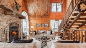 L’intérieur d’une cabane en rondins, avec une cheminée, des murs en bois, un escalier et un coin salon confortable.