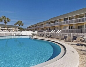 A swimming pool with lounge chairs and a multi-story building with balconies. - Paradise By The Pool, pet friendly, beach chairs and umbrella services. (Destin)