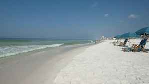 A beach with white sand, a clear blue sky, and a few beach chairs and umbrellas. - Paradise By The Pool, pet friendly, beach chairs and umbrella services. (Destin)