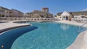 A swimming pool with a white fence, lounge chairs, and a building in the background. - Paradise By The Pool, pet friendly, beach chairs and umbrella services. (Destin)