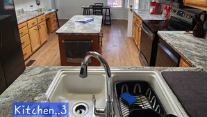 Una cocina con armarios de madera, encimeras de granito, una isla central, un ventilador de techo y vistas al exterior a través de amplios ventanales.