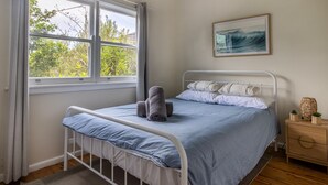 Un dormitori amb un llit, una finestra amb cortines, una taula de nit amb una làmpada i un quadre penjat a la paret.